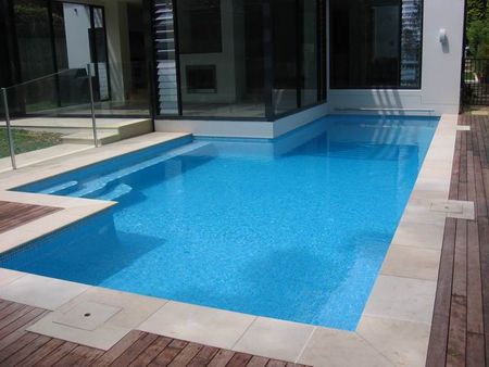 Fully tiled light blue pool with house wall on pool edge
