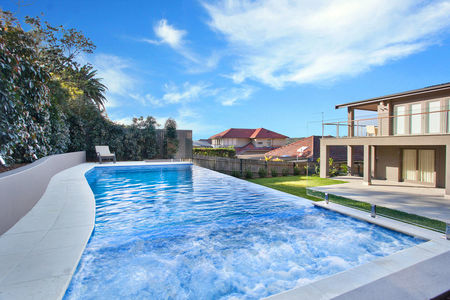 Mid blue fully tiled pool with curved side and spa with jets on and infinity edge