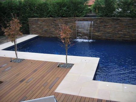 Dark blue tiled pool with decking and feature wall with fountain